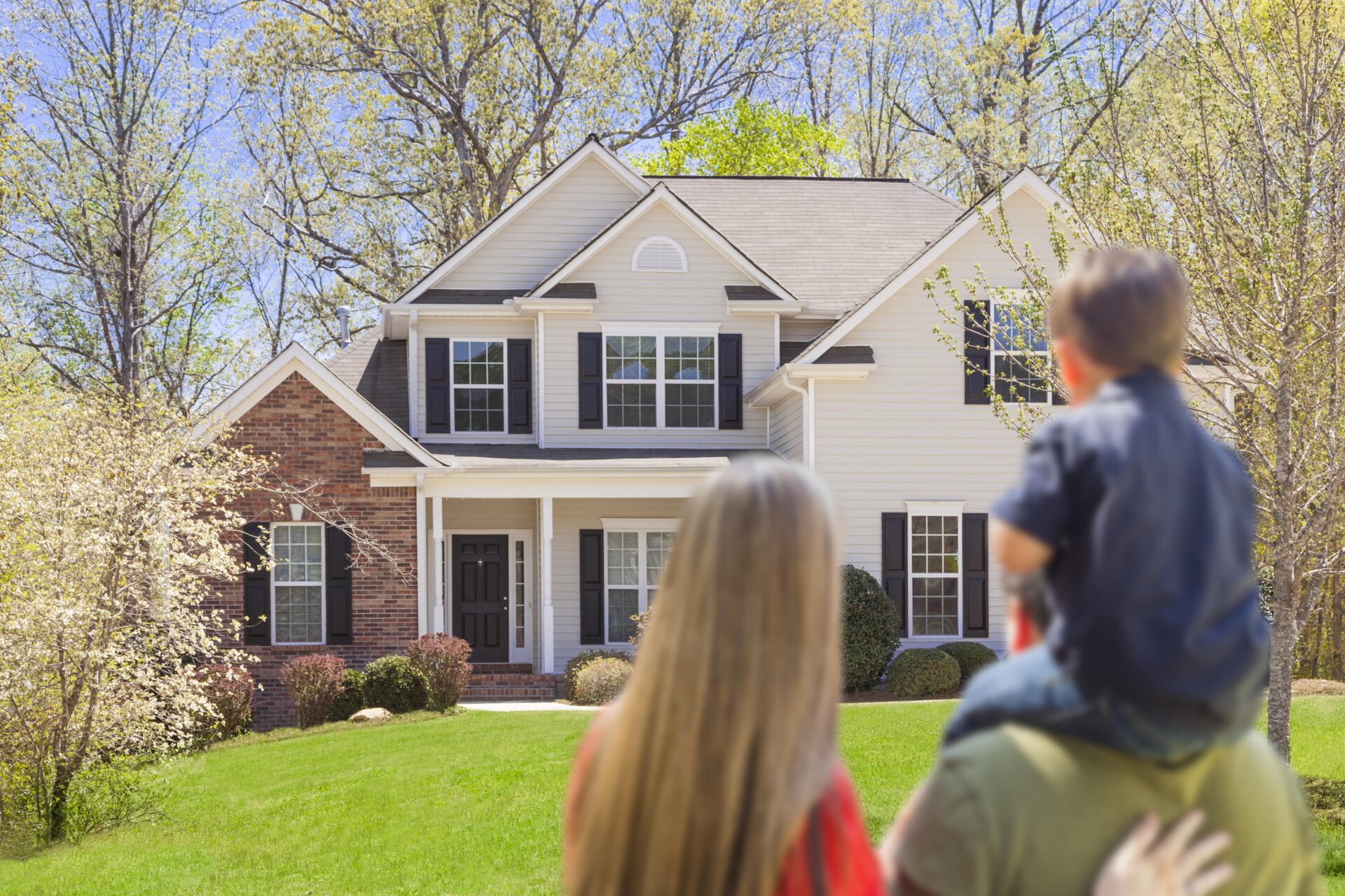 A family of three looks at the exterior of a large home.